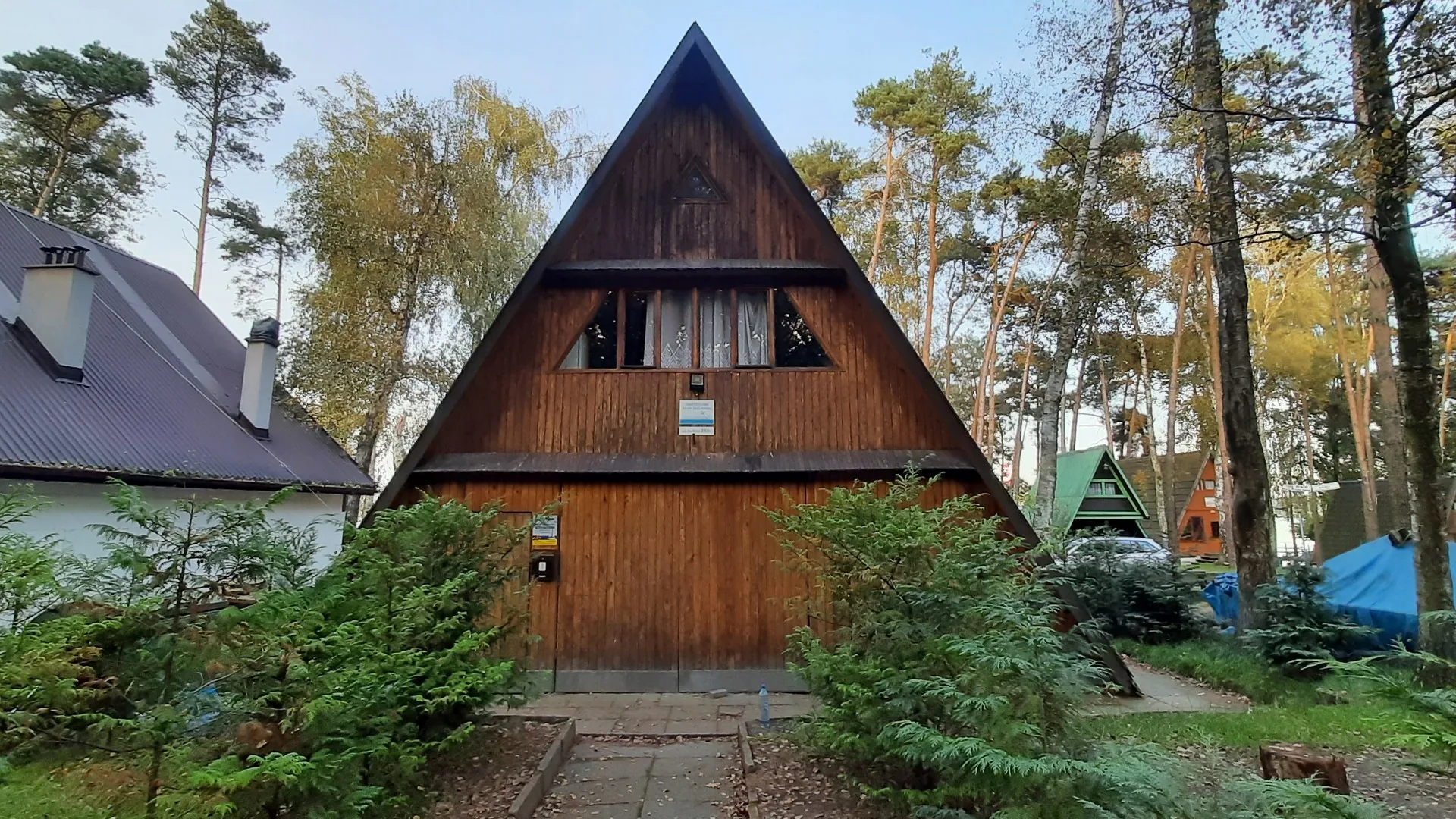 Drewniany domek klubowy z wysokim trójkątnym dachem, otoczony drzewami